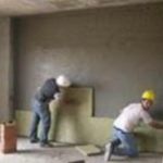 Dos trabajadores instalando paneles aislantes en la pared de una habitación
