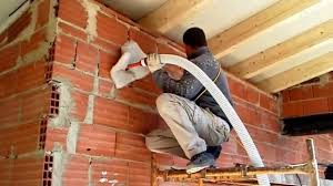 Trabajador aplicando mediante manguera material aislante en pared de ladrillo
