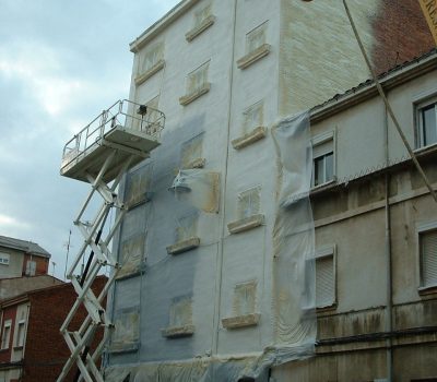 Trabajador en grúa aplicando material aislante en fachada